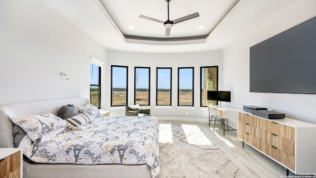 bedroom featuring ceiling fan, a raised ceiling, and light wood-type flooring