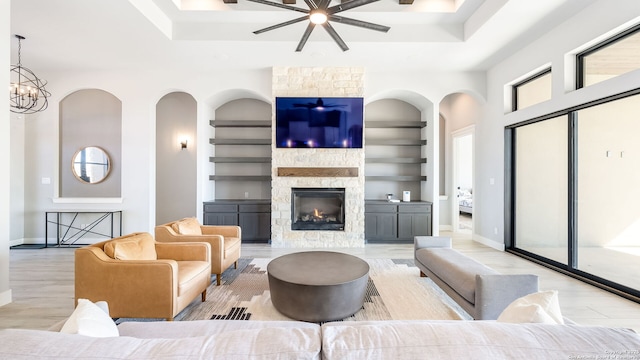 living room with light wood-type flooring, built in features, a stone fireplace, and an inviting chandelier