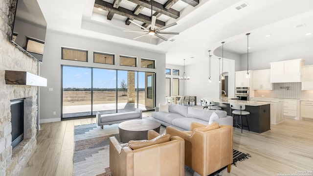 living room featuring ceiling fan with notable chandelier, a high ceiling, a fireplace, light hardwood / wood-style floors, and sink