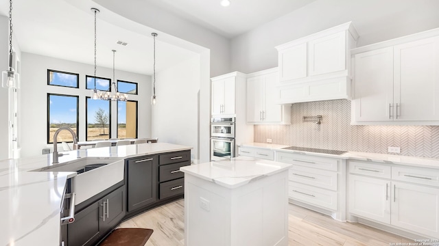 kitchen featuring black electric stovetop, white cabinets, a kitchen island, sink, and double oven