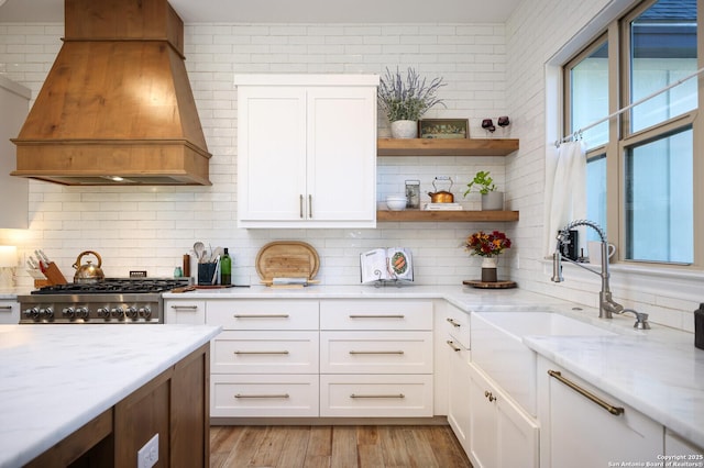 kitchen featuring custom range hood, stove, decorative backsplash, white cabinets, and light stone counters