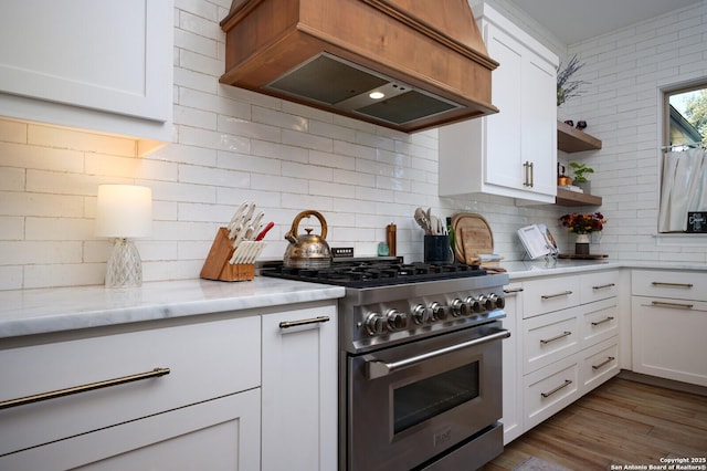 kitchen featuring light stone countertops, white cabinetry, custom range hood, backsplash, and high end stainless steel range