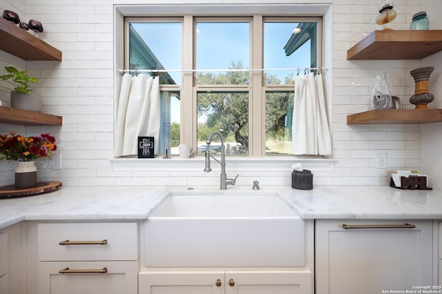 kitchen featuring sink, light stone counters, white cabinets, and tasteful backsplash