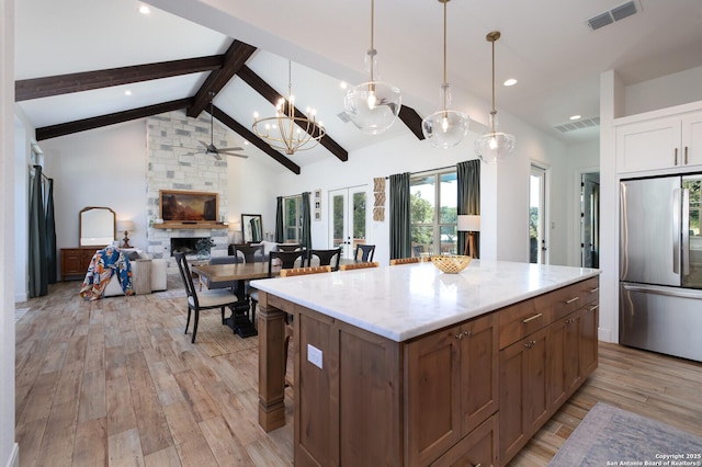 kitchen with a fireplace, light hardwood / wood-style floors, hanging light fixtures, stainless steel fridge, and beam ceiling