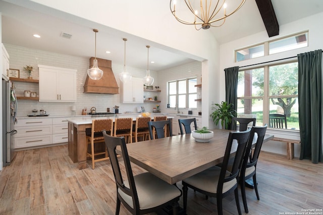 dining space with light hardwood / wood-style flooring, a chandelier, and vaulted ceiling with beams