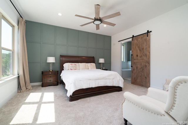 carpeted bedroom featuring ceiling fan, ensuite bathroom, and a barn door