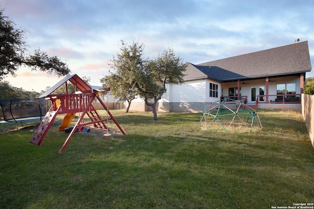 playground at dusk featuring ceiling fan, a lawn, and a trampoline