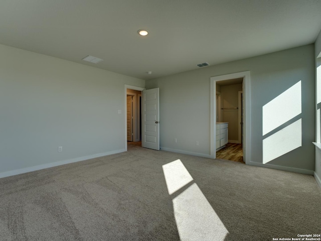 unfurnished bedroom with a spacious closet, light carpet, and ensuite bath