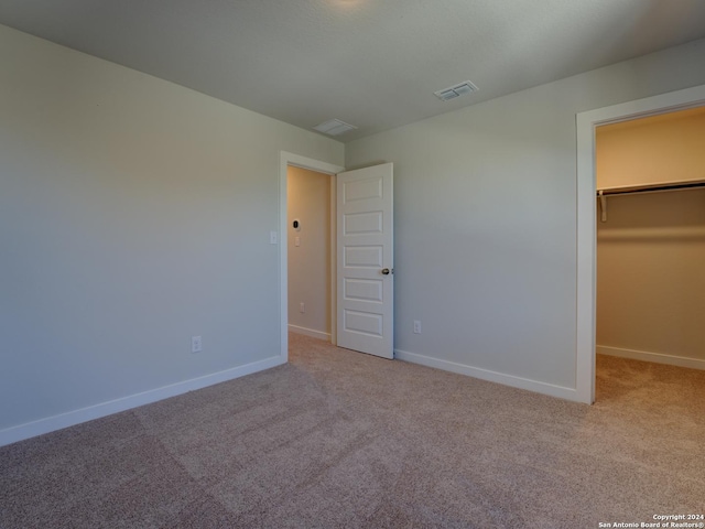 unfurnished bedroom featuring a walk in closet, light carpet, and a closet