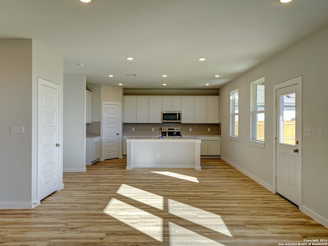 kitchen with appliances with stainless steel finishes, backsplash, white cabinets, light wood-type flooring, and a kitchen island with sink