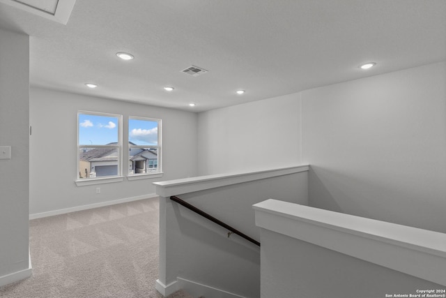 hallway featuring light colored carpet and a textured ceiling