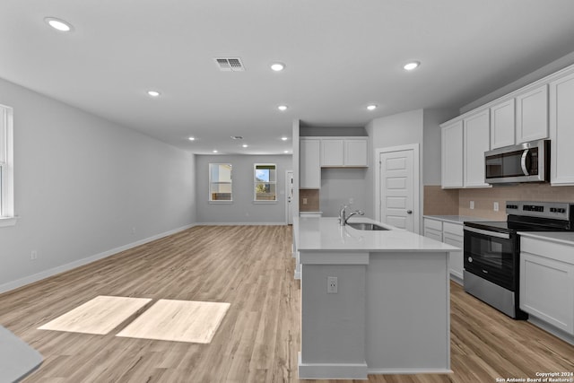 kitchen with appliances with stainless steel finishes, an island with sink, sink, white cabinets, and light hardwood / wood-style flooring