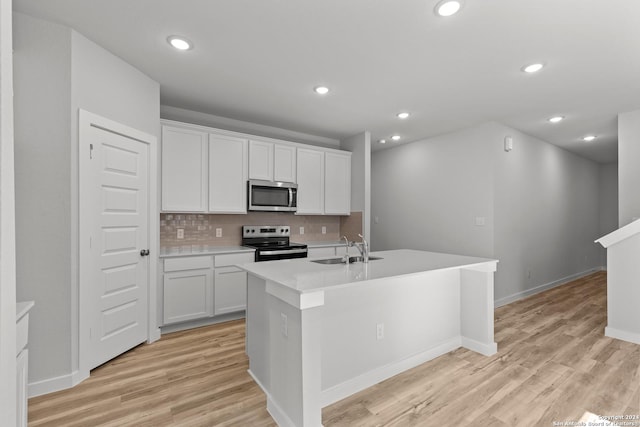 kitchen with appliances with stainless steel finishes, white cabinetry, sink, decorative backsplash, and a kitchen island with sink