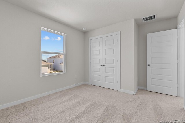 unfurnished bedroom with light colored carpet and a closet