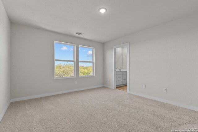 unfurnished bedroom featuring light colored carpet and ensuite bath