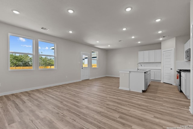 kitchen featuring sink, light hardwood / wood-style flooring, appliances with stainless steel finishes, a kitchen island with sink, and white cabinets
