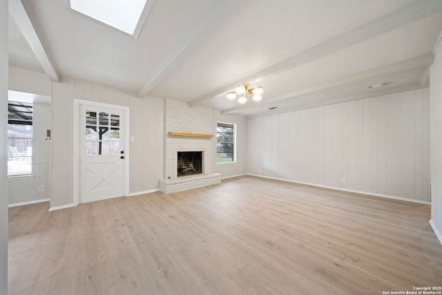 unfurnished living room with a skylight, beamed ceiling, light hardwood / wood-style floors, and a fireplace