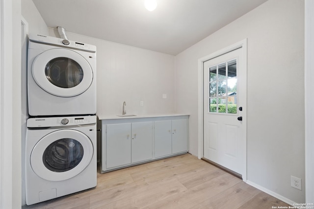 laundry room featuring light hardwood / wood-style floors, cabinets, stacked washer and clothes dryer, and sink