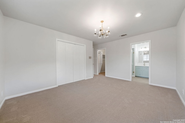 unfurnished bedroom with a closet, connected bathroom, an inviting chandelier, and light carpet