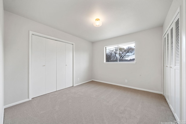 unfurnished bedroom featuring light carpet and two closets