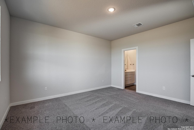 unfurnished bedroom with dark carpet, ensuite bathroom, and a textured ceiling