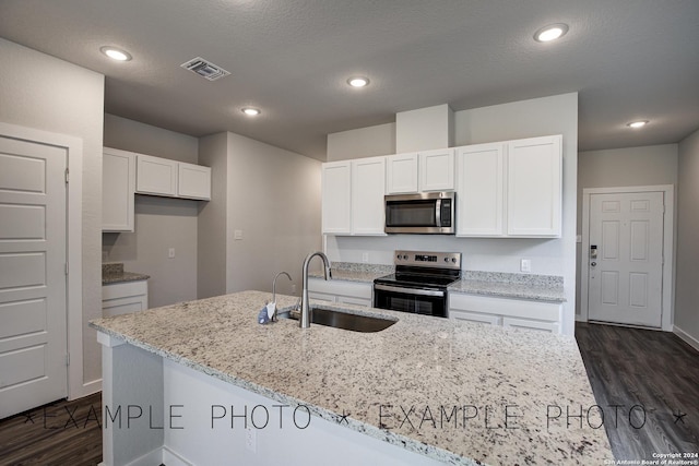 kitchen with appliances with stainless steel finishes, sink, white cabinets, light stone countertops, and a kitchen island with sink