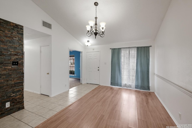 tiled empty room featuring vaulted ceiling and a notable chandelier