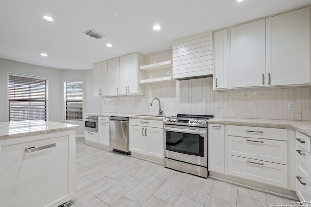 kitchen with sink, white cabinetry, appliances with stainless steel finishes, light stone countertops, and decorative backsplash