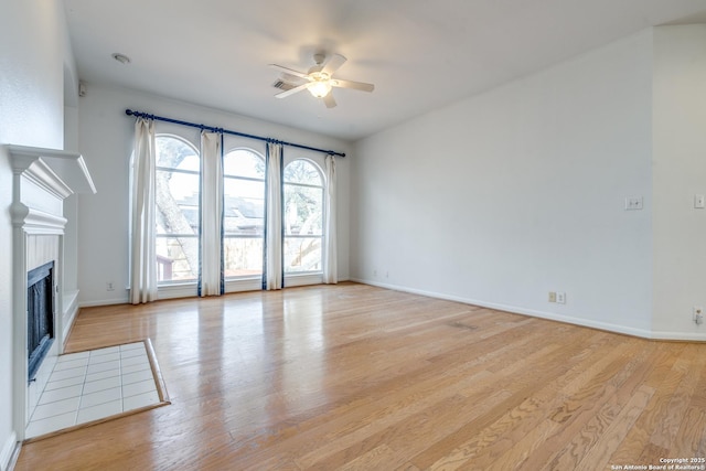 unfurnished living room with ceiling fan, a tiled fireplace, and light wood-type flooring