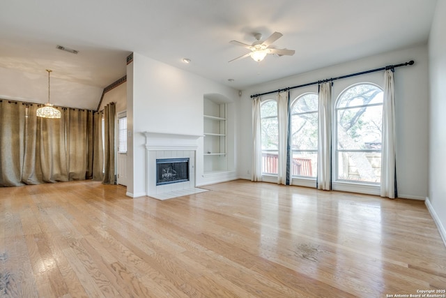 unfurnished living room with a fireplace, built in shelves, ceiling fan, and light wood-type flooring