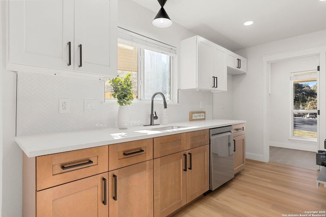 kitchen with sink, white cabinetry, backsplash, light hardwood / wood-style floors, and stainless steel dishwasher