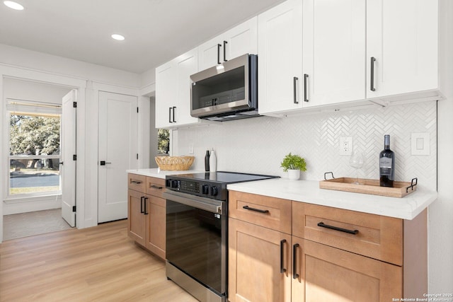 kitchen with appliances with stainless steel finishes, tasteful backsplash, white cabinets, light stone counters, and light hardwood / wood-style floors