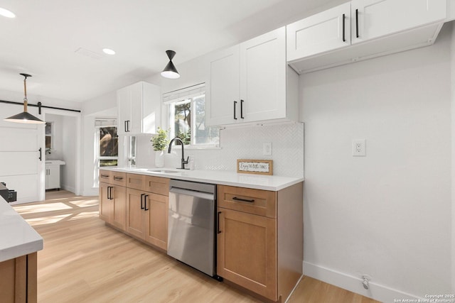 kitchen with white cabinetry, hanging light fixtures, dishwasher, a barn door, and light hardwood / wood-style floors