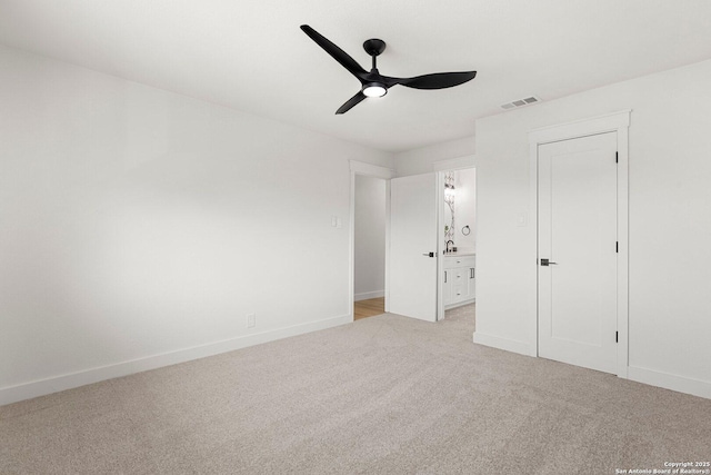 unfurnished bedroom with ensuite bath, light colored carpet, a closet, and ceiling fan