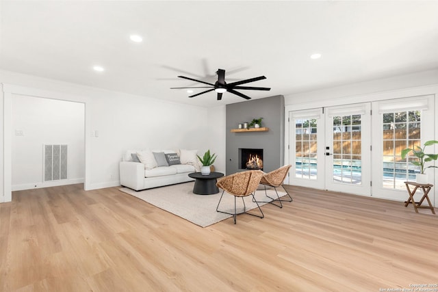 living room featuring a fireplace, french doors, ceiling fan, and light wood-type flooring