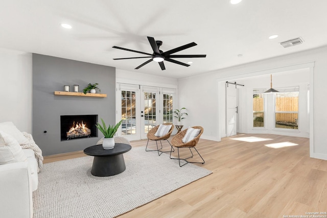 living room with ceiling fan, a barn door, light wood-type flooring, and french doors