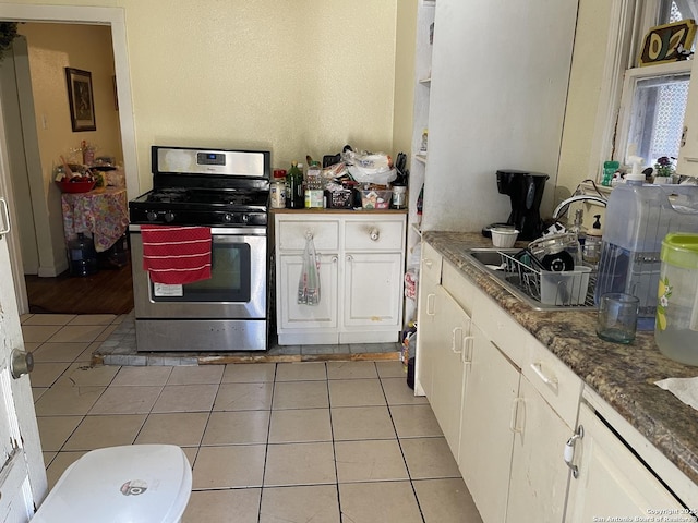 kitchen with sink, stainless steel range with gas cooktop, light tile patterned floors, and white cabinetry