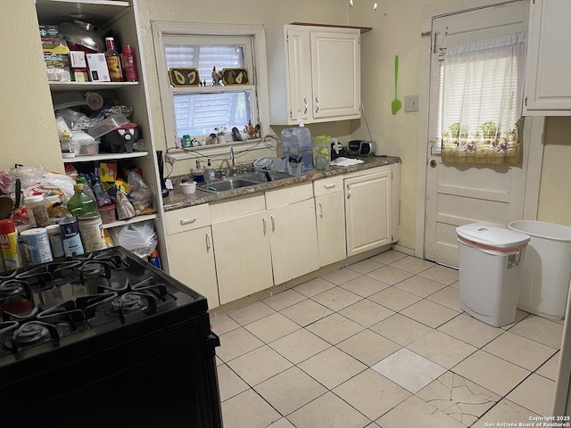 kitchen featuring sink, black stove, white cabinetry, and light tile patterned flooring