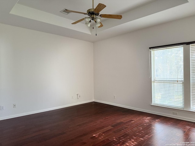 unfurnished room with ceiling fan, dark hardwood / wood-style floors, and a tray ceiling