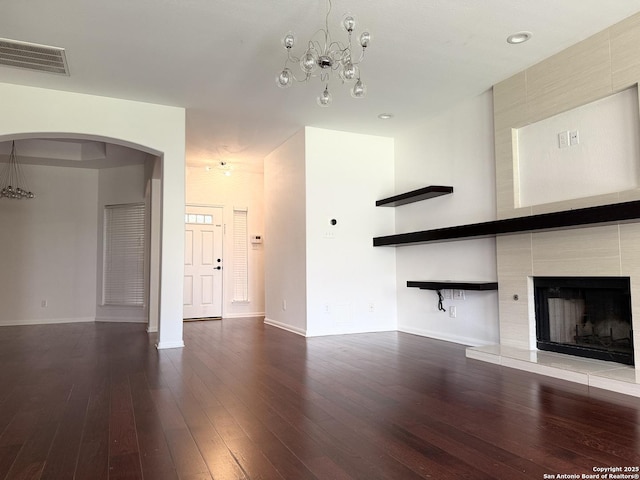 unfurnished living room with hardwood / wood-style flooring, a chandelier, and a tiled fireplace