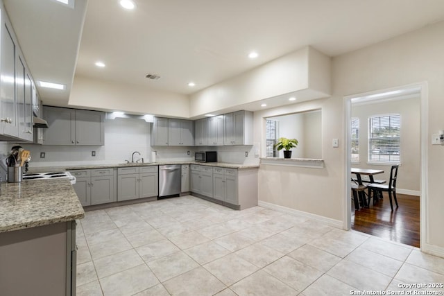 kitchen featuring light stone countertops, light tile patterned floors, stainless steel dishwasher, sink, and gray cabinets