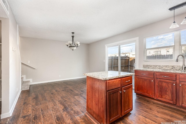 kitchen featuring sink, light stone countertops, hanging light fixtures, and a kitchen island