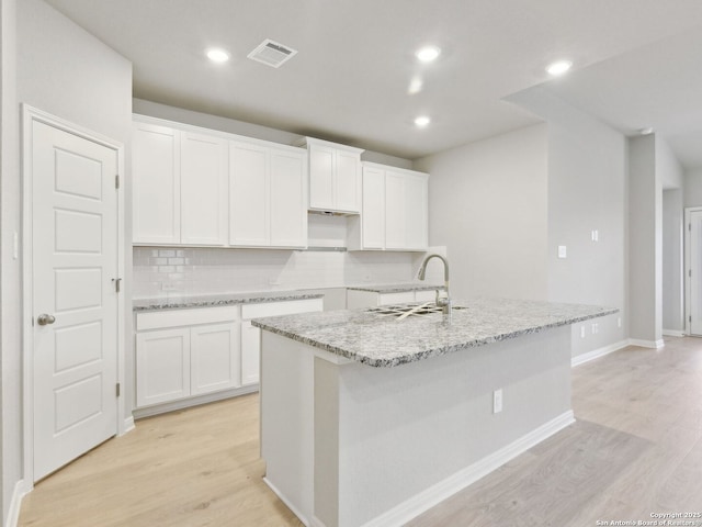 kitchen with white cabinets, tasteful backsplash, sink, light hardwood / wood-style flooring, and a center island with sink