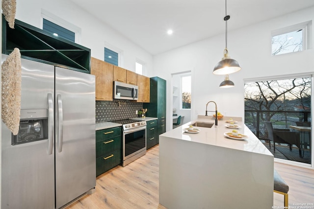 kitchen featuring appliances with stainless steel finishes, decorative backsplash, sink, hanging light fixtures, and a kitchen island with sink