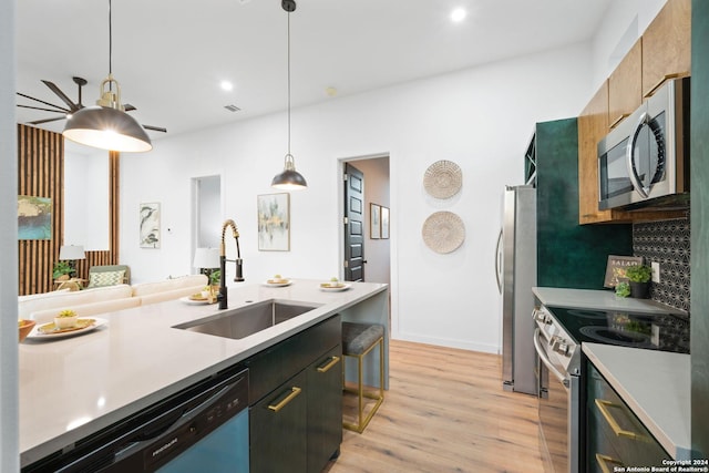 kitchen with light hardwood / wood-style floors, appliances with stainless steel finishes, tasteful backsplash, hanging light fixtures, and sink