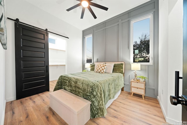 bedroom with light wood-type flooring, multiple windows, ceiling fan, and a barn door