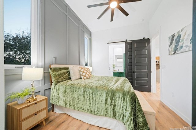 bedroom with ceiling fan, a barn door, and wood-type flooring