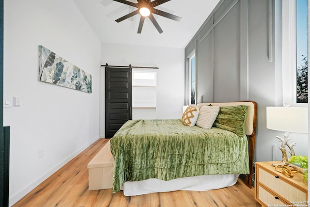 bedroom featuring ceiling fan, a barn door, hardwood / wood-style floors, and lofted ceiling