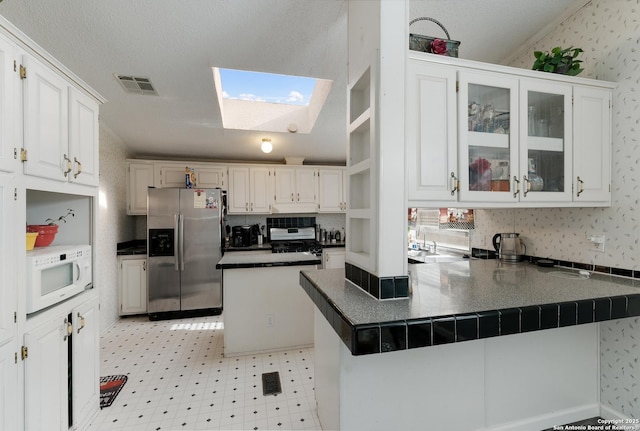 kitchen with kitchen peninsula, white cabinets, a textured ceiling, a skylight, and stainless steel appliances