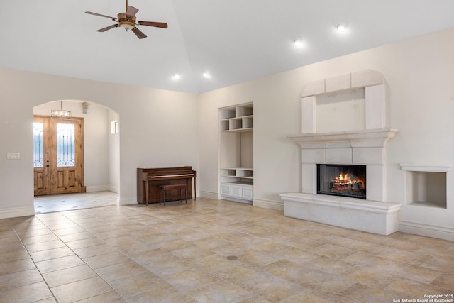 unfurnished living room featuring ceiling fan, built in shelves, lofted ceiling, and a fireplace